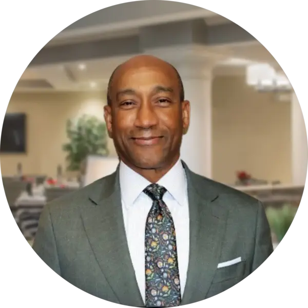 Smiling man in a gray suit and floral tie in an office setting, cropped circular portrait